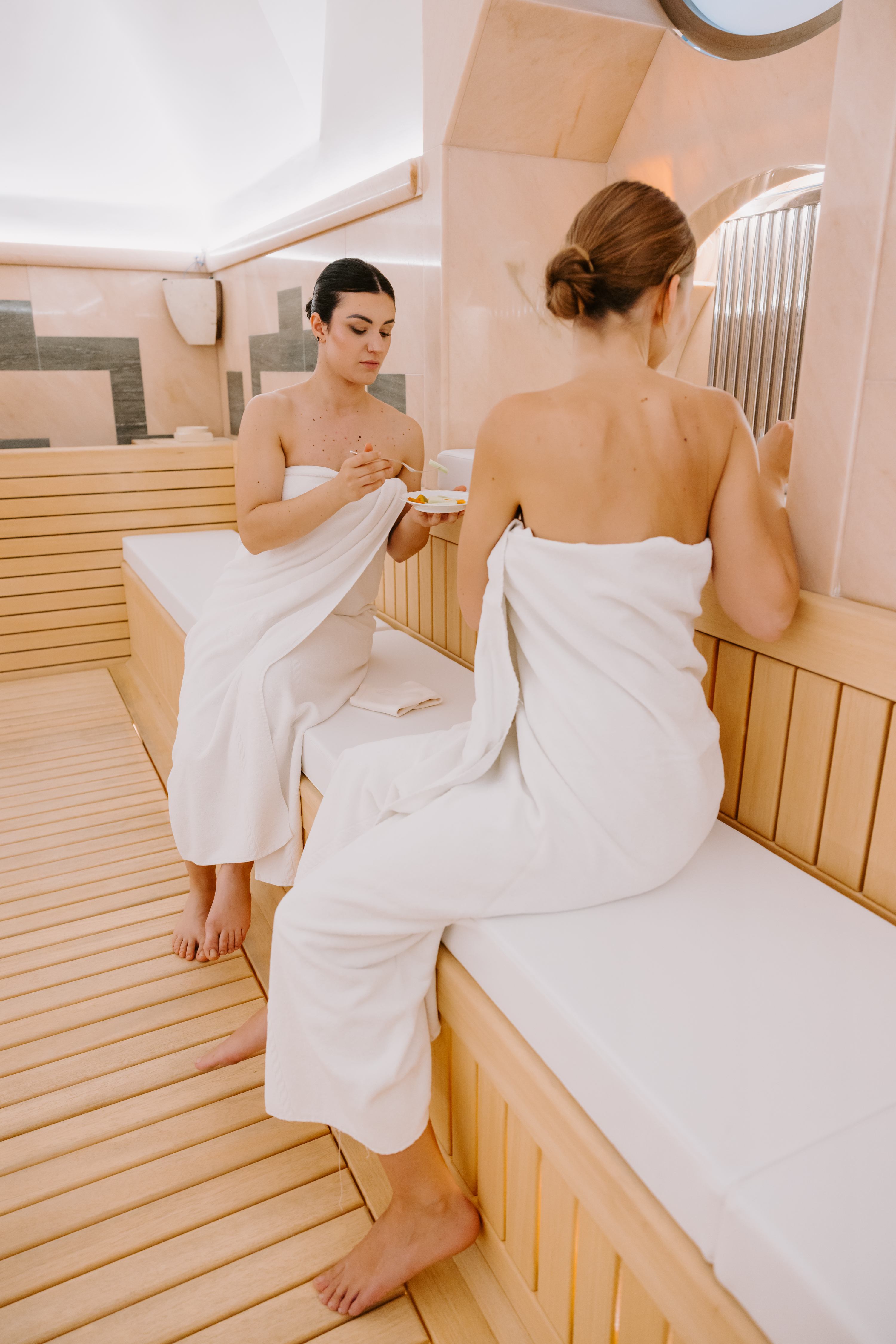 Due donne in sauna con asciugamani bianchi che bevono tisana
