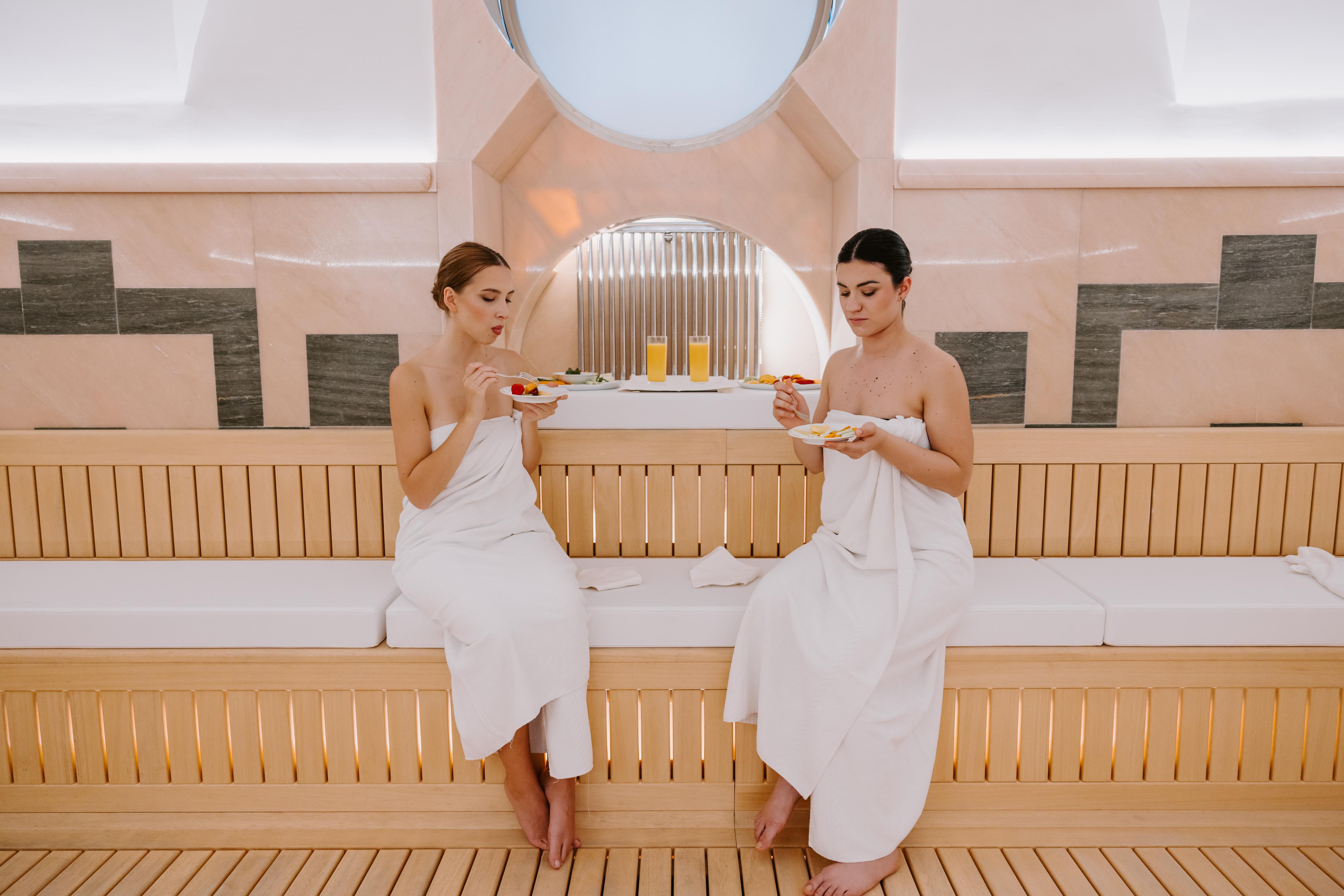 Due donne in asciugamani bianchi che gustano snack nell'area relax